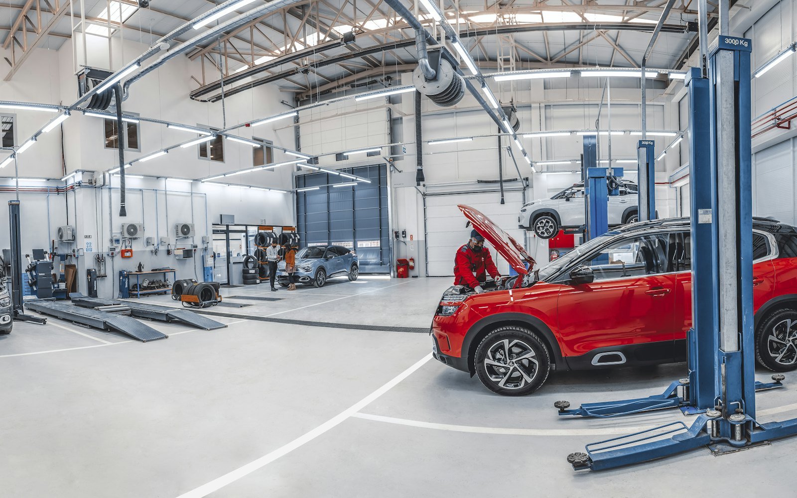 Helle Werkstatthalle mit vier Hebebühnen, ein roter SUV steht angehoben